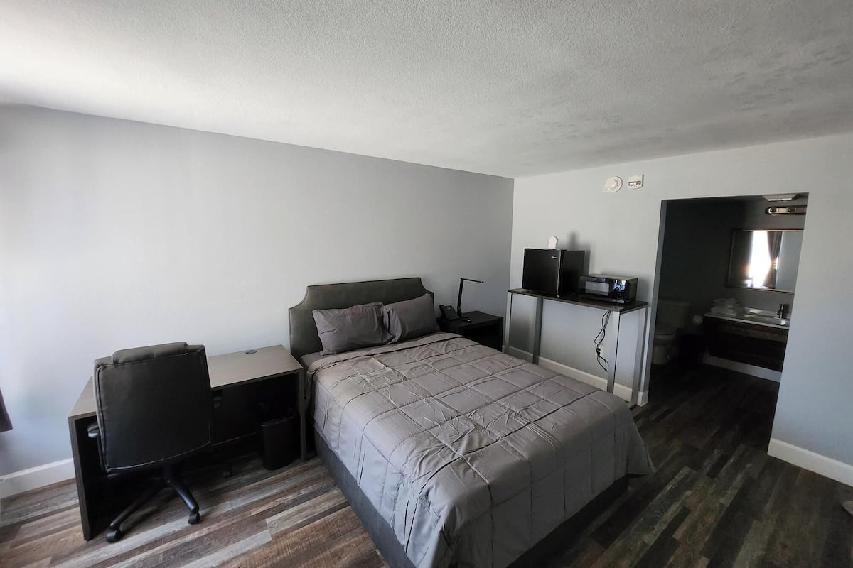 Een compacte hotelkamer met een bed, een bureau, een stoel, een kleine kitchenette en een badkamer.