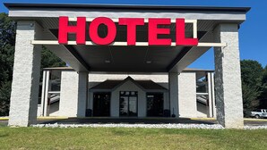 Entrada de un hotel con un llamativo letrero que dice 'HOTEL', un área de acceso cubierta y fachada de piedra.
