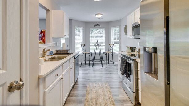 A modern kitchen with white cabinetry, a stainless steel refrigerator, a built-in oven, and a dining area with two chairs. - Cozy North Carolina Abode - Minutes from Downtown! (Mount Holly)