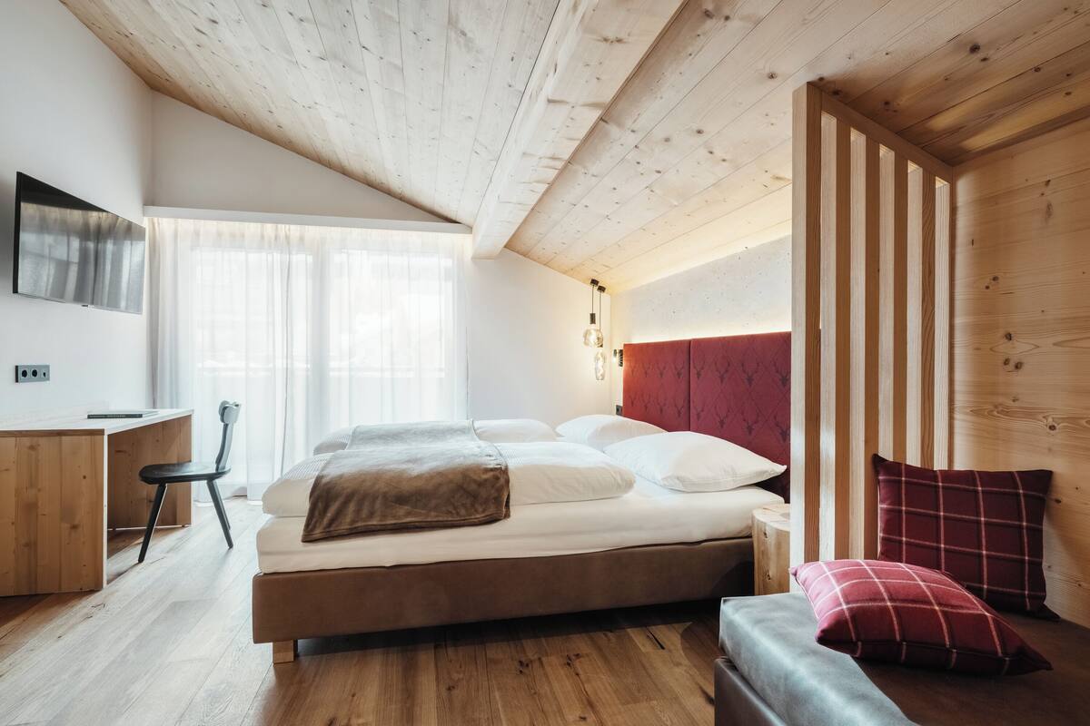 Quarto moderno com teto de madeira, cama com roupa de cama branca, escrivaninha e cadeira.