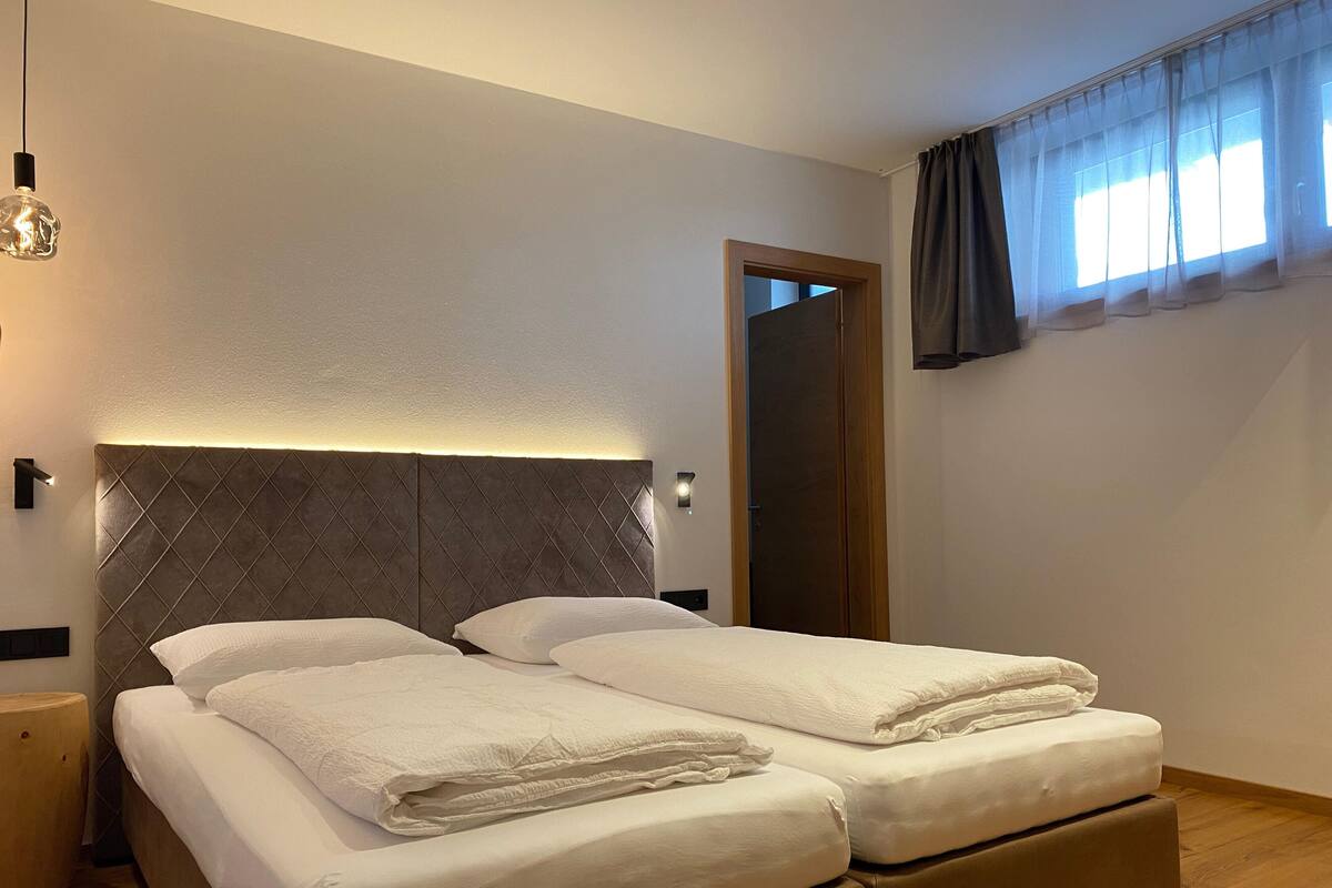 Uma cama de casal com cabeceira acolchoada, uma mesinha de cabeceira e um espelho na parede.