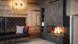 A modern living room with a wooden wall panel, a black sofa with patterned cushions, a fireplace, and a shelf with decorative items. - Villa Trieste (Corvara in Badia)