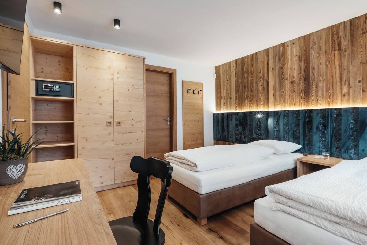 Quarto moderno com guarda-roupa de madeira, cama com roupa de cama branca, mesa de cabeceira e escrivaninha com cadeira.