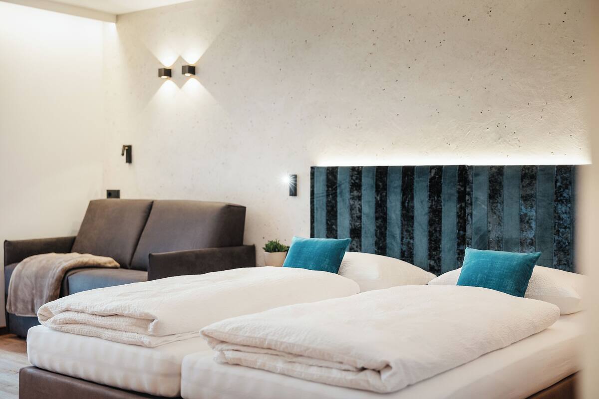 Quarto de hotel com duas camas, um sofá e uma luminária fixada na parede.