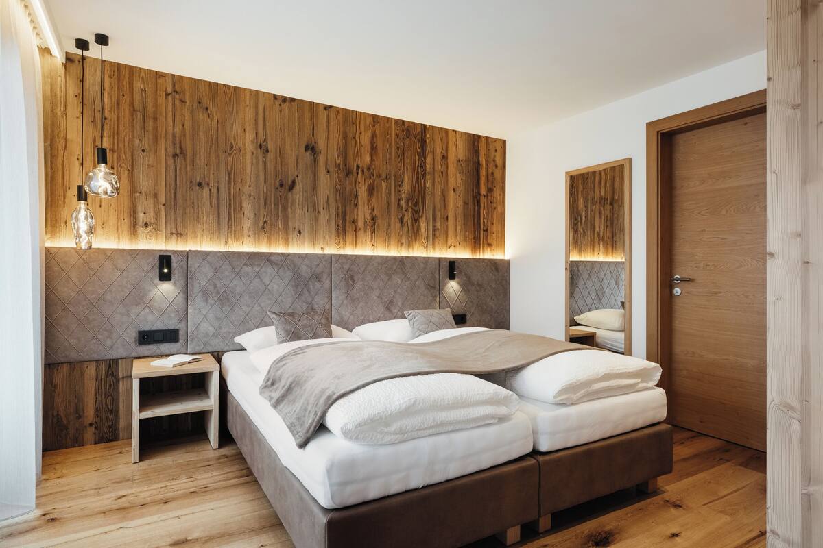 Quarto moderno com cabeceira de madeira, mesa de cabeceira, cama com roupa de cama branca e porta de madeira.