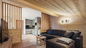 A modern living room with a dark brown sofa, wooden flooring, a TV, and a small wooden table. - Villa Trieste (Corvara in Badia)