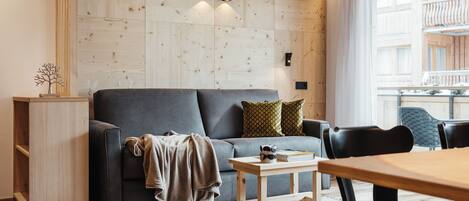 A modern living room with a grey sofa, wooden panel walls, a small wooden table, and a view of a balcony.