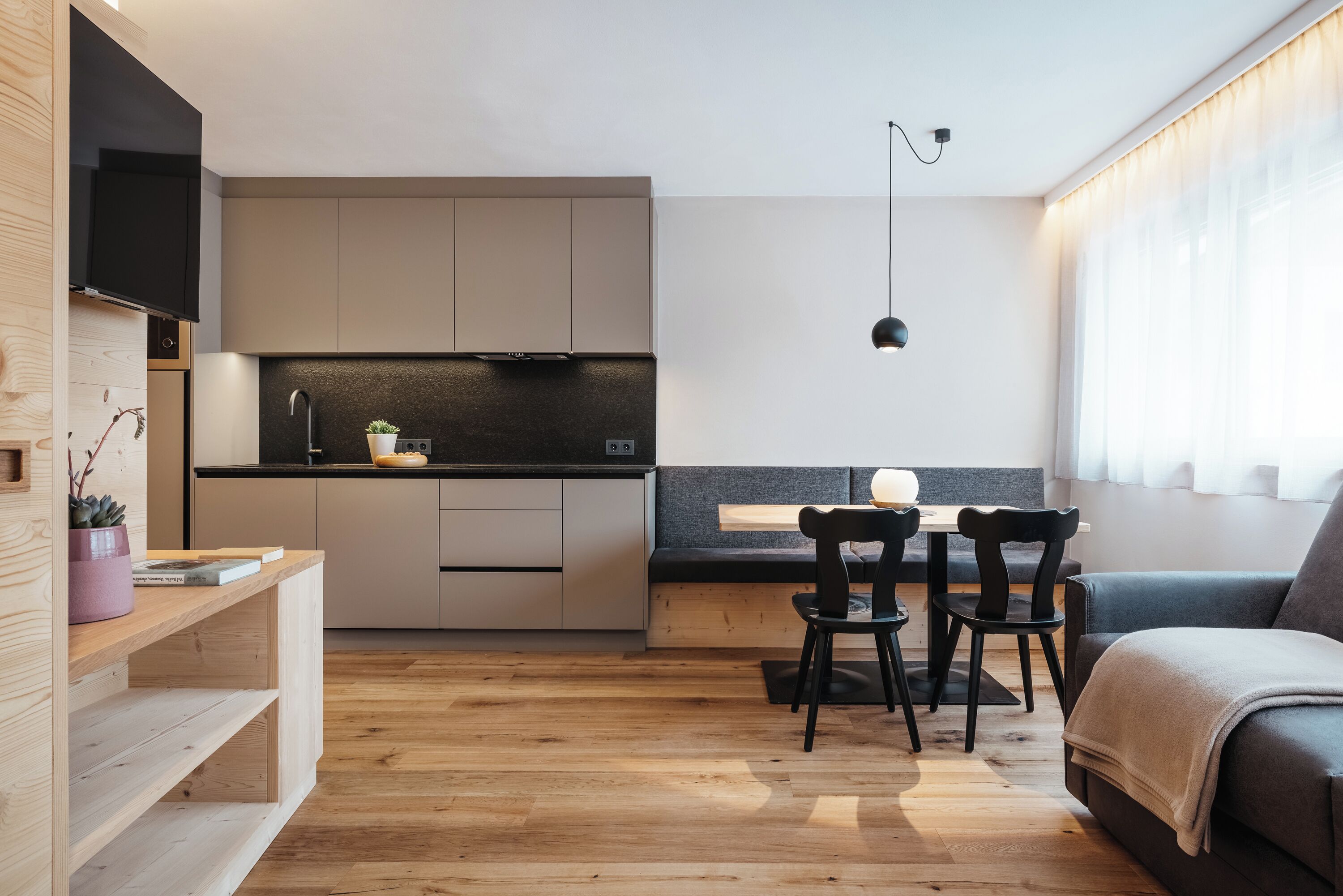 Un espace de vie compact comprenant un coin cuisine, un coin repas avec deux chaises, un canapé et une grande fenêtre avec des rideaux.
