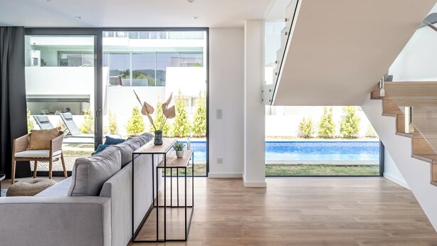 Un salon moderne avec un canapé, une table à manger et une vue sur une piscine et un espace verdoyant.
