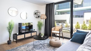 Un salon moderne doté d’un téléviseur à écran plat, d’un canapé, d’une table basse ronde et d’une grande fenêtre donnant sur l’extérieur.