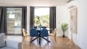 Un espace repas moderne avec une table en verre, des chaises bleues et une vue sur la verdure environnante.