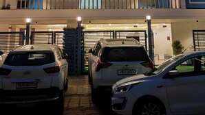 Un hôtel à plusieurs étages, doté d’un design moderne, comprenant des balcons, un café avec terrasse et un parking pouvant accueillir plusieurs voitures.