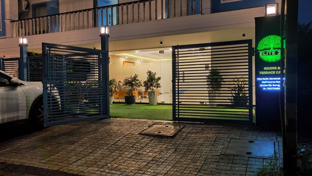 Une entrée fermée par un portail mène à un hôtel. Une enseigne indique « ELITE 2 » et « CHAMBRES ET TERRASSE ».