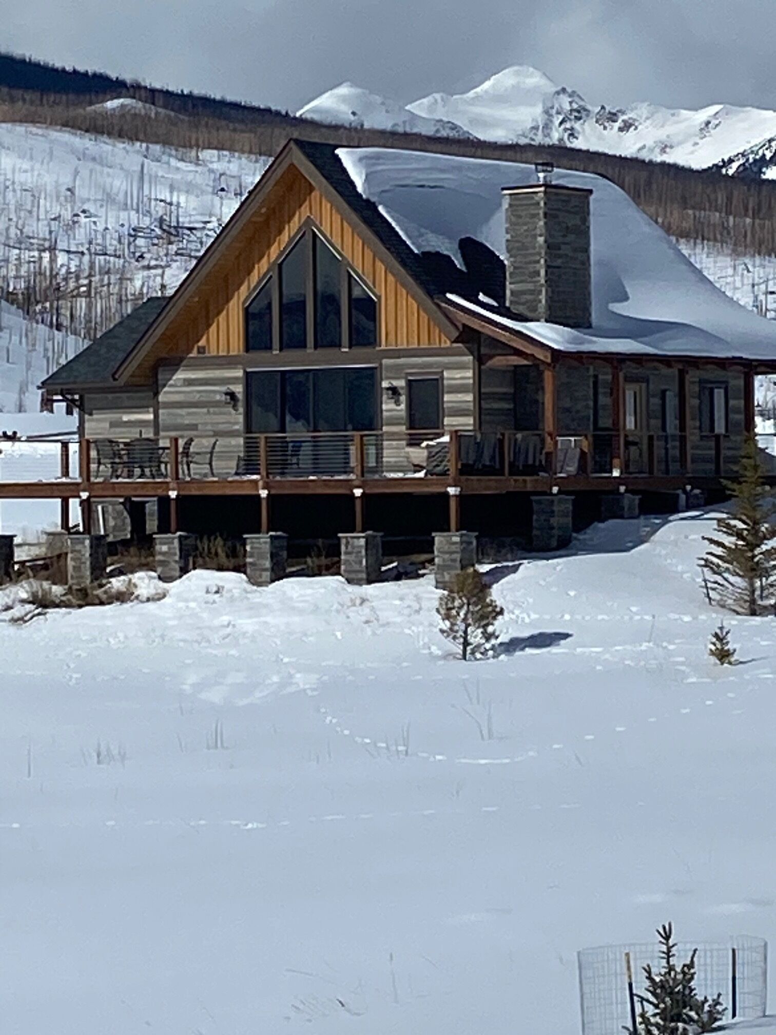 Une cabane en rondins dotée d’une grande terrasse, entourée de neige et de montagnes.
