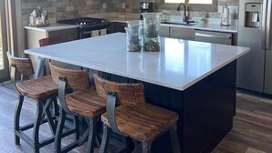 Une cuisine moderne dotée d’un grand îlot central, de tabourets de bar et d’une cuisinière intégrée.