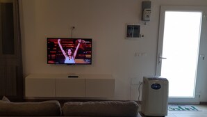 A living room with a television mounted on the wall, a white cabinet below it, and a large window to the right. - Beautiful renovated house (Mirano)