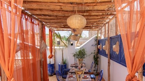 An outdoor dining area with a thatched roof, blue chairs, and orange curtains. - Riad Karim (Marrakech)
