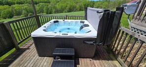Ein Whirlpool auf einer Holzterrasse mit Blick auf eine grüne Landschaft.