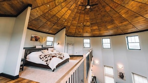 A spacious bedroom with a wooden ceiling, a large bed, a balcony, and multiple windows.