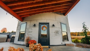 A cylindrical metal building with a black door, two windows, and a wooden roof.