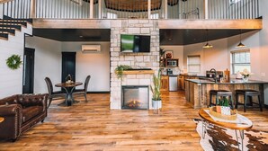 A spacious living area with a stone fireplace, a wooden ceiling, and a kitchen area with a bar.