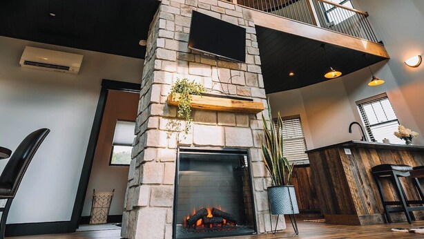 A spacious interior with a high ceiling, a stone fireplace, a balcony, and a large window.