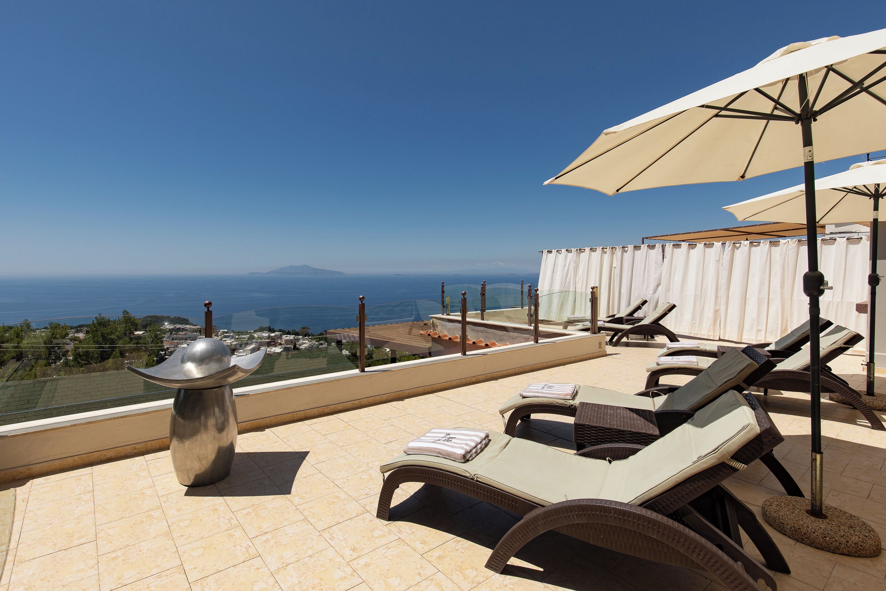 Terraço no telhado com cadeiras de lounge, uma mesa e guarda-sóis, com vista para o mar.
