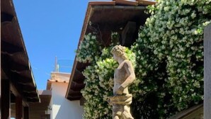Un patio con una estatua de piedra, plantas en macetas y suelo de baldosas.