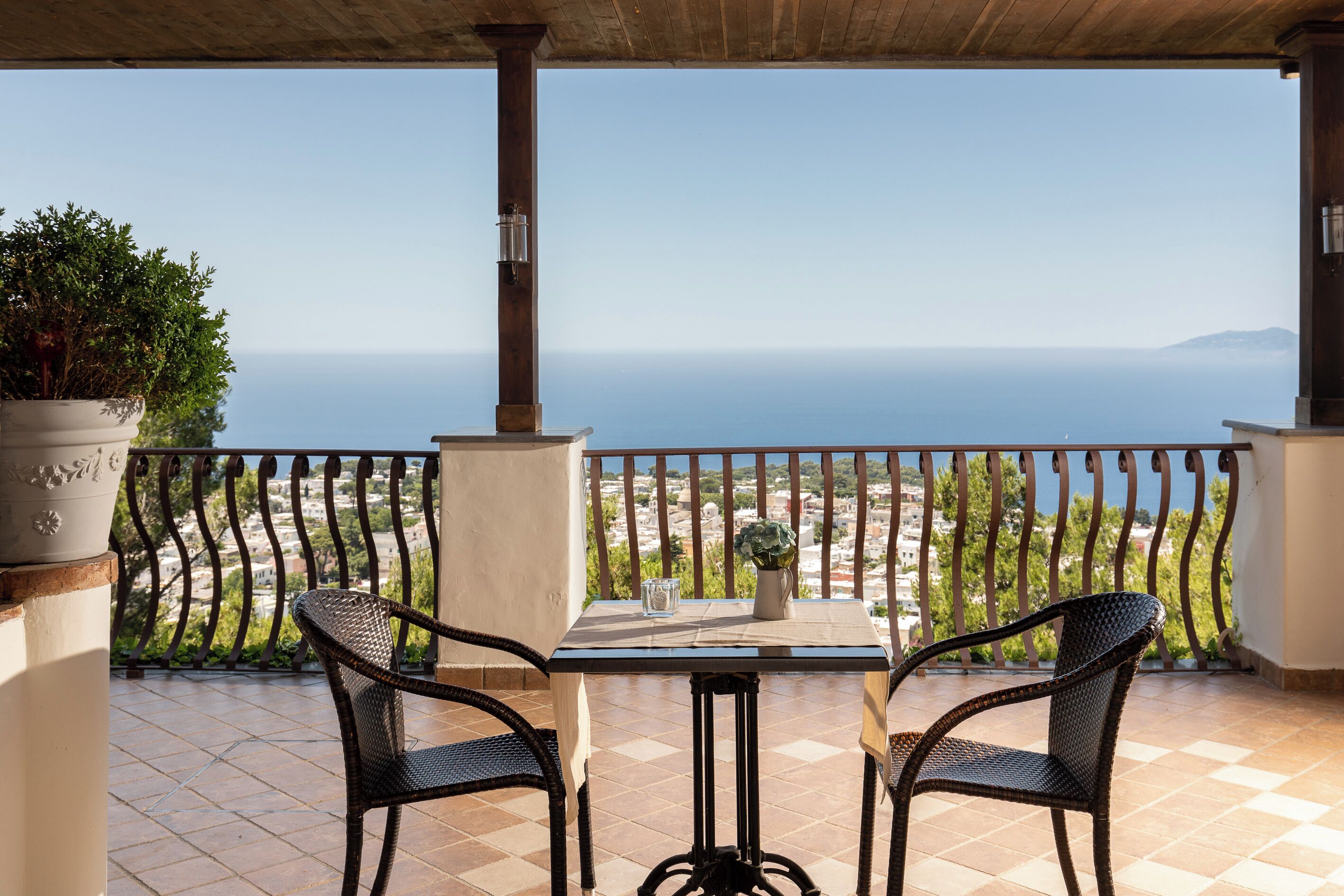 Ein Balkon mit zwei Korbstühlen, einem Tisch und einem Blumentopf.
