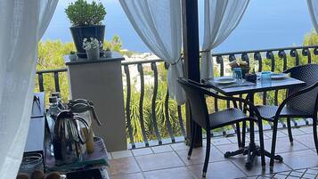 Un patio al aire libre con mesa lista para comer, una planta en maceta y vista al mar.