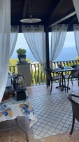 Un patio al aire libre con mesa lista para comer, una planta en maceta y vista al mar.