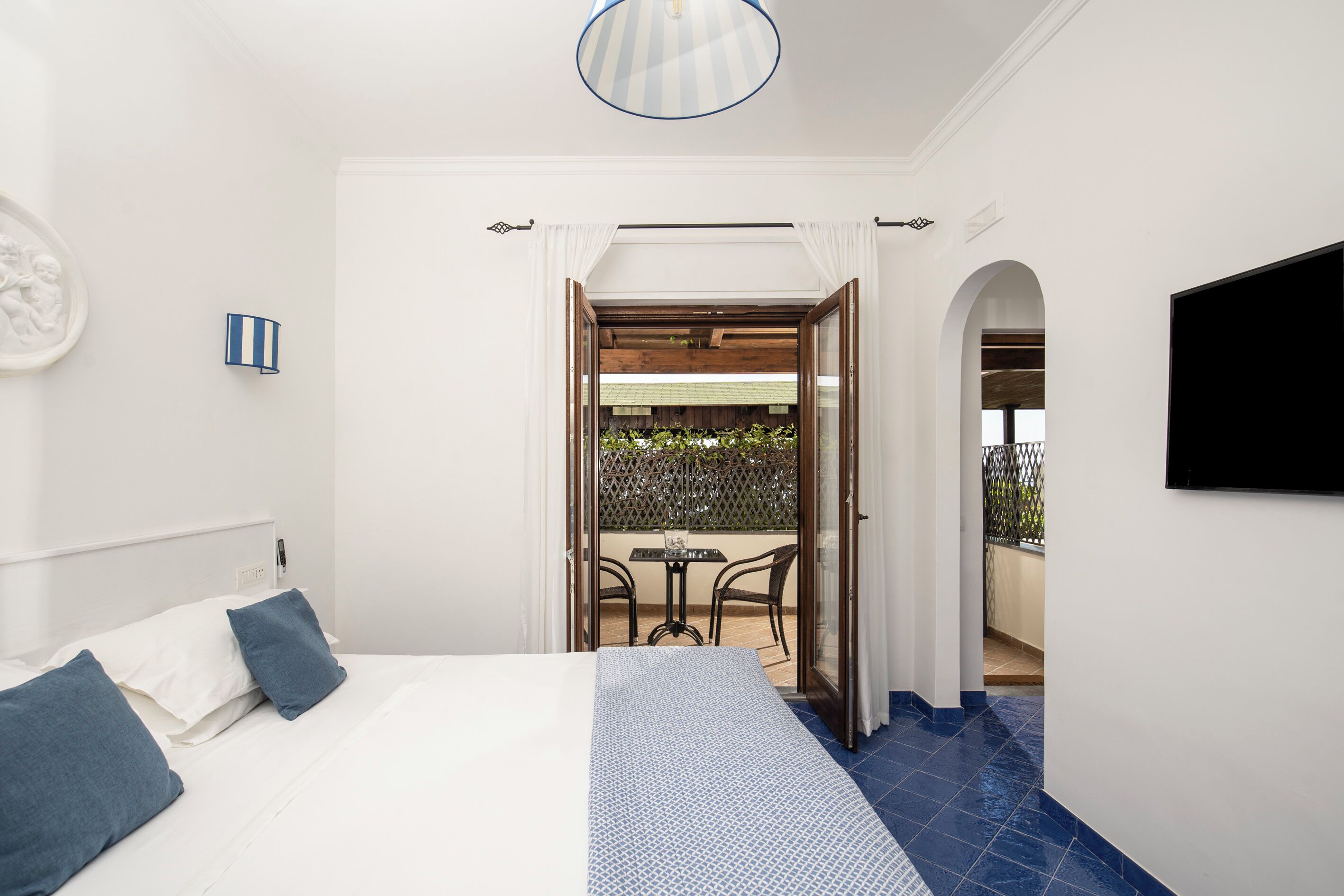 Habitación de hotel con cama, televisor, una mesita con sillas y balcón con vistas.