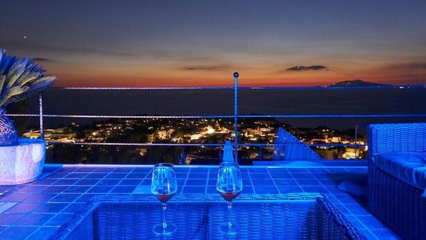 Una terraza con dos copas de vino vacías, una planta en maceta y vista a un paisaje urbano al anochecer.