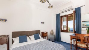 Un dormitorio con cama, escritorio, silla, ventana con cortinas y vista al mar.