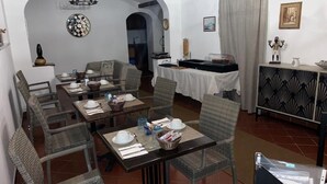 Un comedor con sillas de mimbre, una mesa redonda con mantel blanco y una araña.