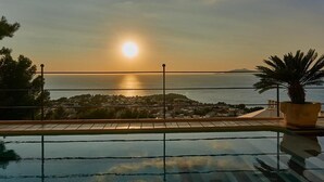 Una piscina con vista al mar y un pueblo lejano al atardecer.