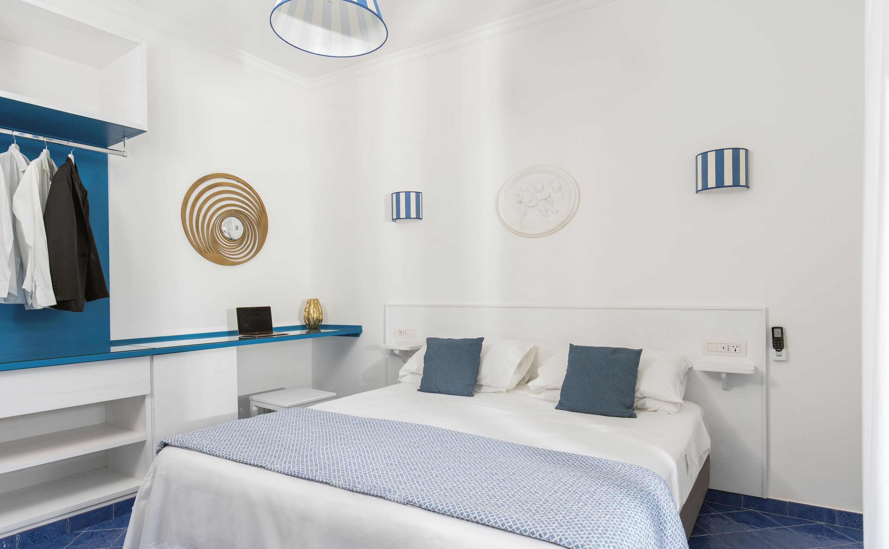 A modern hotel room with a bed, a vanity with a mirror, a blue shelf, and a blue patterned bedspread.