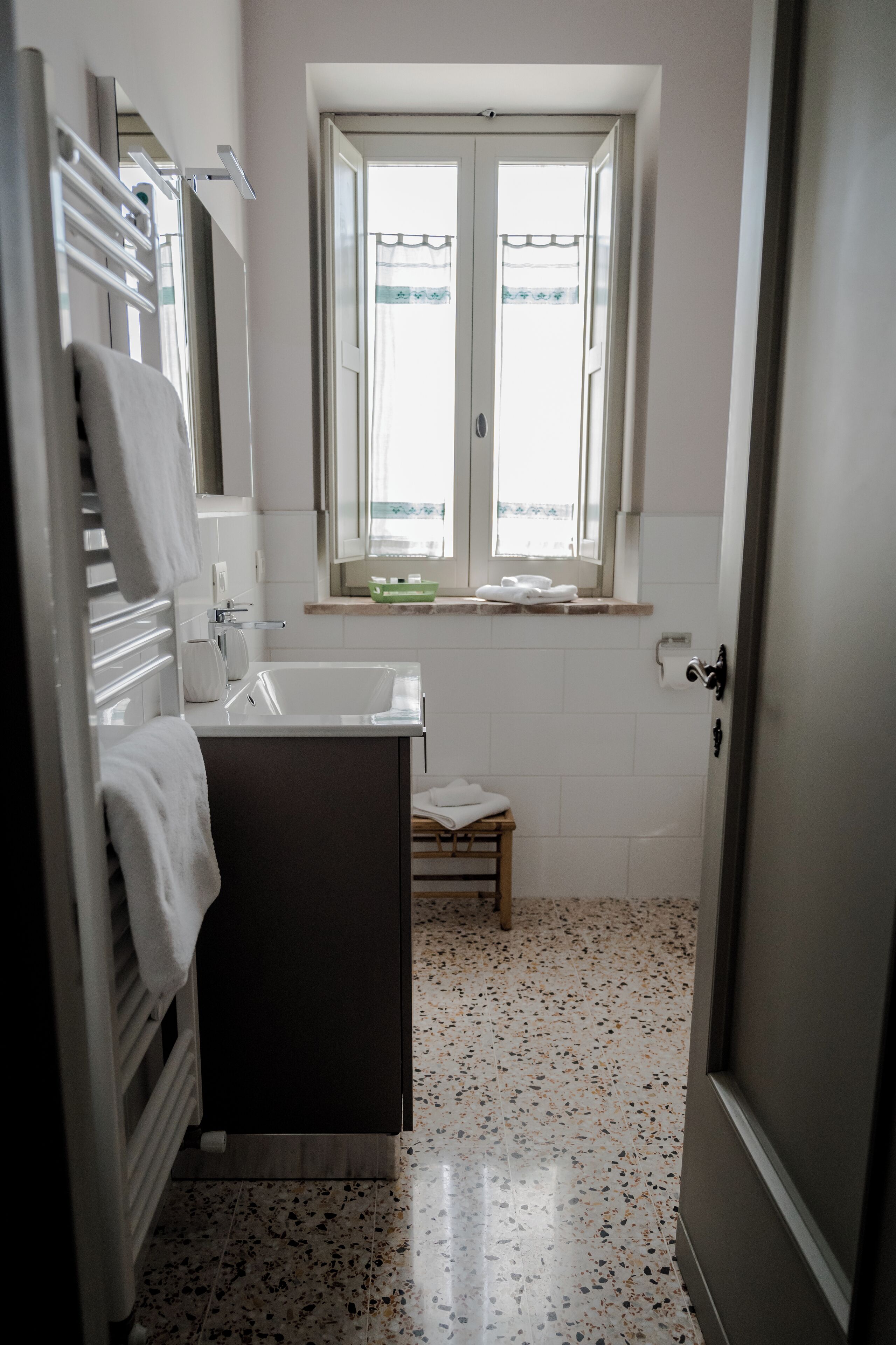 Een badkamer met een witte wastafel, een spiegel, een raam met uitzicht en een handdoekhouder.