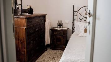 A bedroom with a bed, a wooden dresser, a nightstand, and a wall-mounted light fixture.