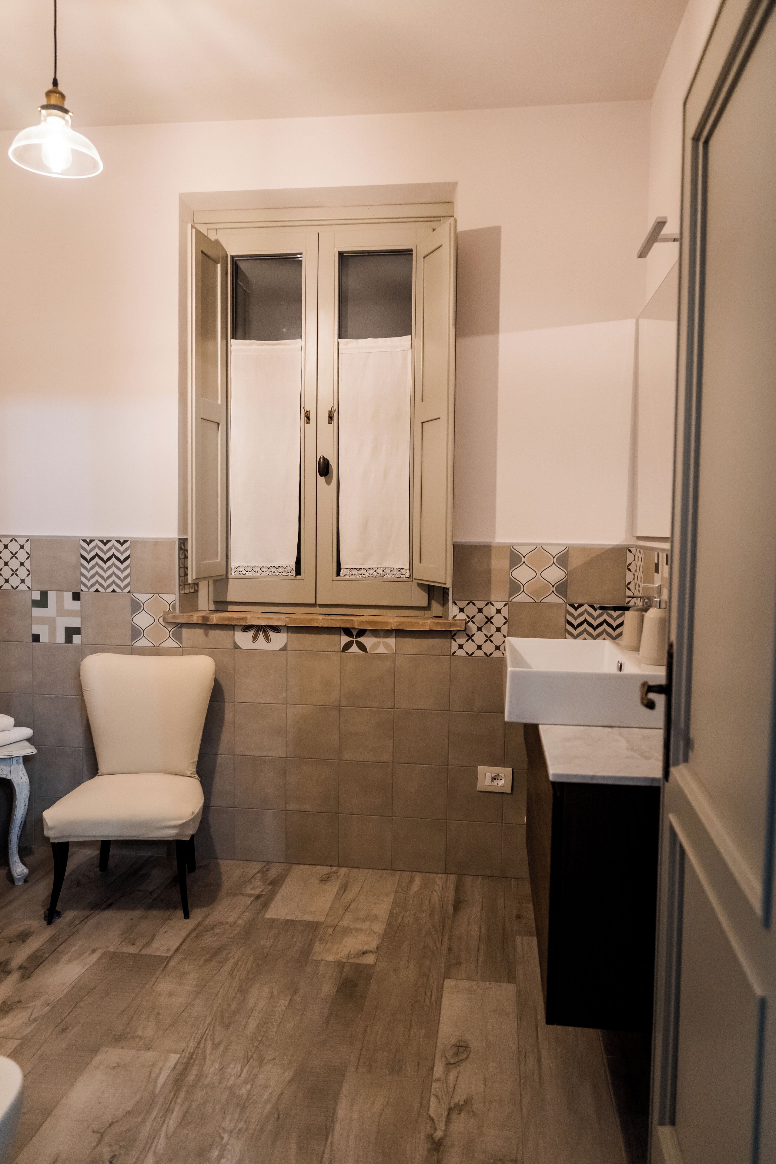 Une salle de bain avec un plancher en bois, une chaise blanche, un lavabo et un miroir.