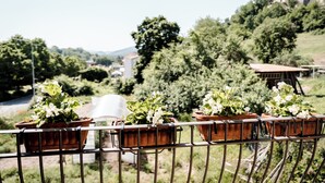 Un balcón con macetas y plantas, con vista a un paisaje verde exuberante con árboles y un edificio al fondo.