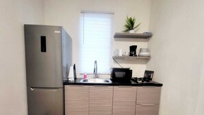 A compact kitchen with a refrigerator, sink, microwave, and a small shelf with kitchen items. - D'lujo Apt. #2 con A/C, Wi-Fi & Parking (Vega Baja)