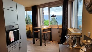 A kitchen with a built-in oven, a dining table with stools, a large window with a view, and a stand mixer on the counter.