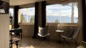 A room with a large window, a piano, a chair, and a table.