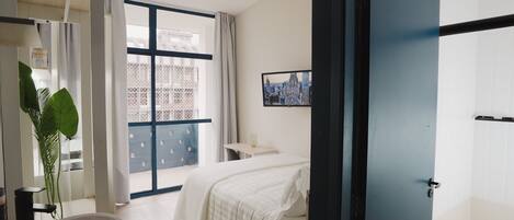 Un dormitorio moderno con una cama grande, una mesita de noche, un espejo y vistas al exterior a través de un amplio ventanal.