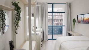 A modern hotel room with a large bed, a desk, a bathroom, and a balcony with a city view. - Apê Metrô Paraíso (São Paulo)