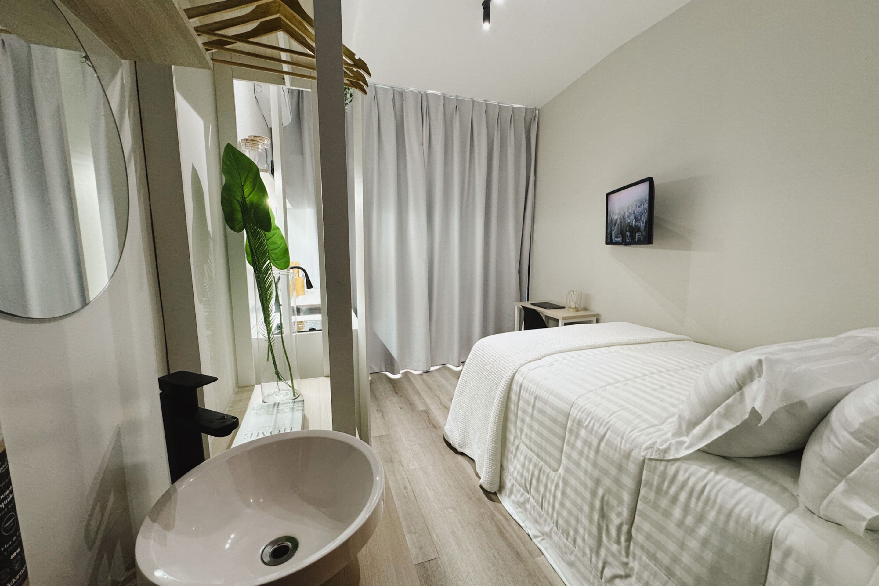 Habitación de hotel moderna con una cama grande, un lavamanos redondo y vistas de la ciudad a través de cortinas translúcidas.
