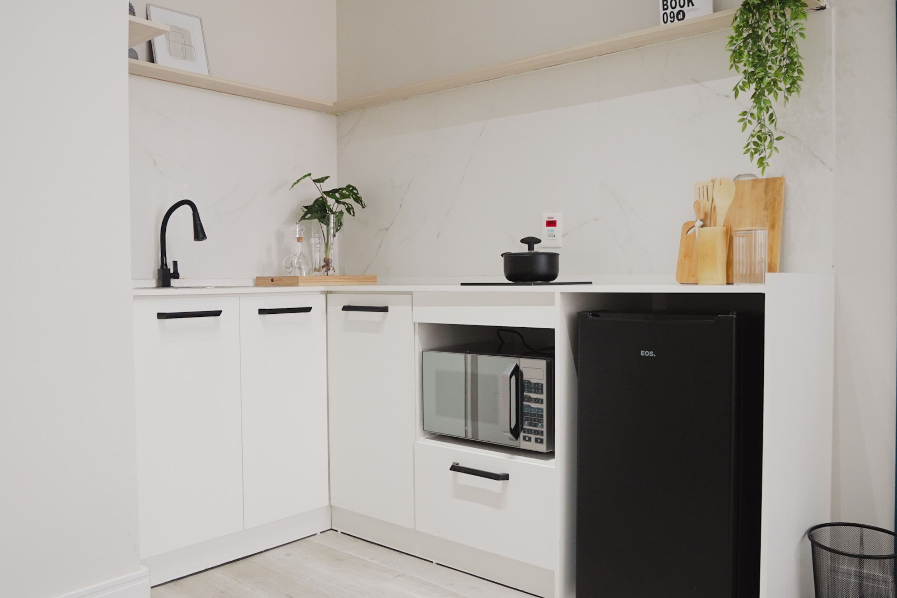 A modern kitchen with white cabinets, a black refrigerator, a microwave, and a black faucet.