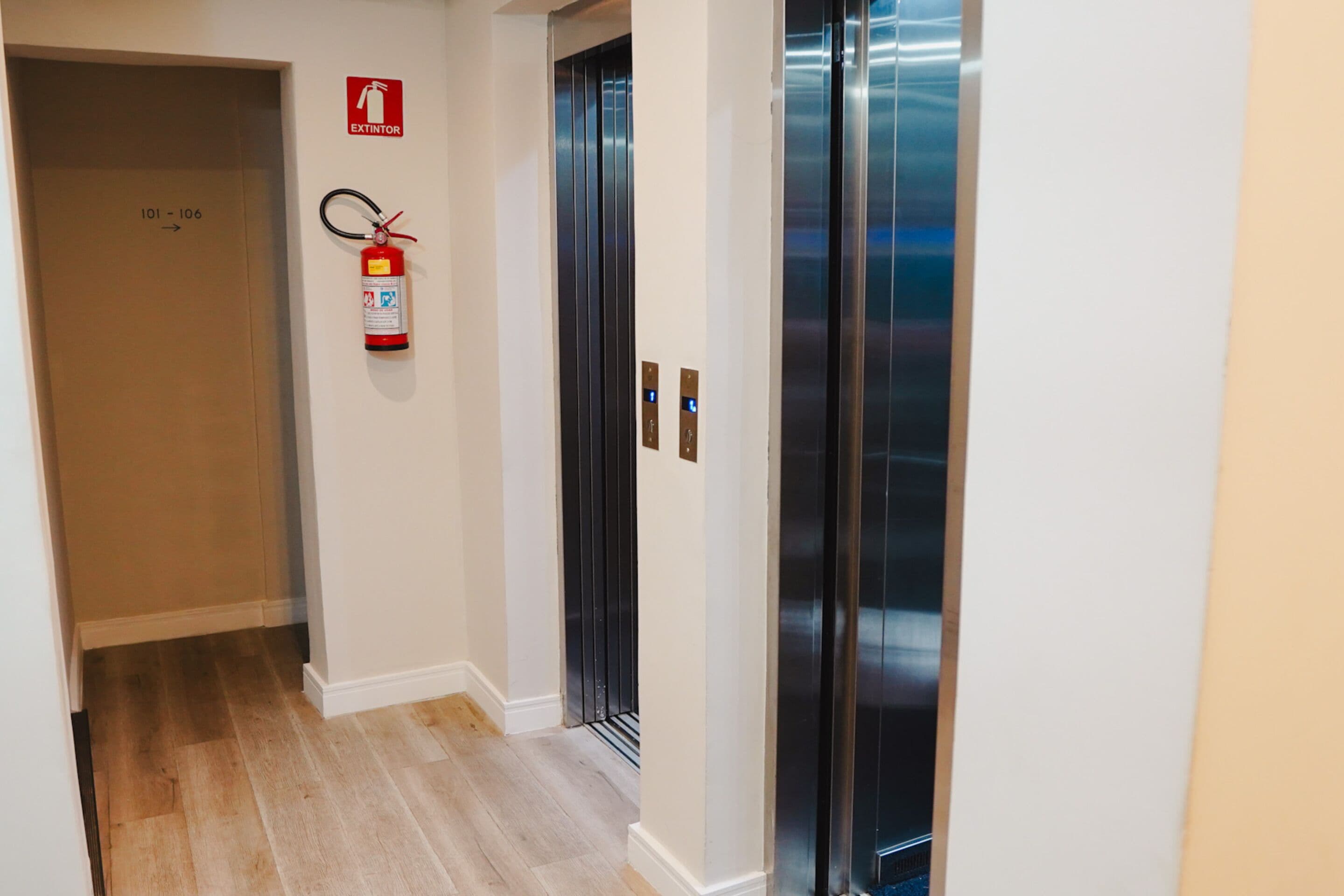 A hallway with an elevator, a fire extinguisher, and a door marked 101-106.