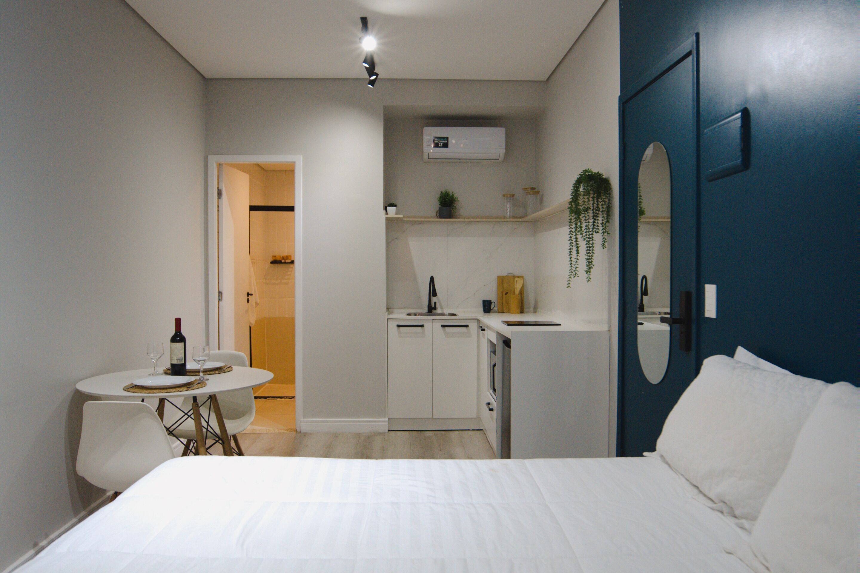 A compact bedroom with a bed, a small dining table with chairs, a kitchenette with a sink and cabinets, and a bathroom with a toilet and shower.